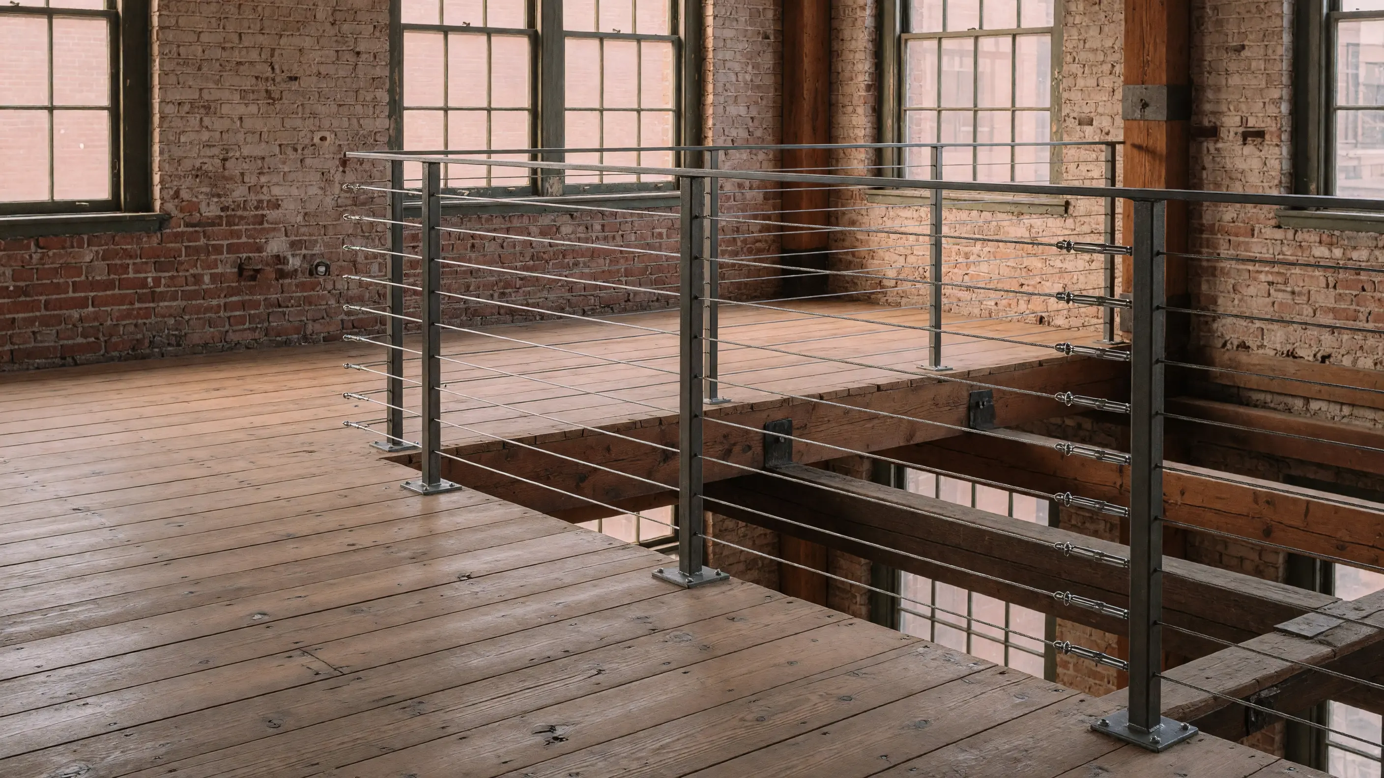 Steel-post cable guardrail edging an open loft mezzanine above a warm industrial living space