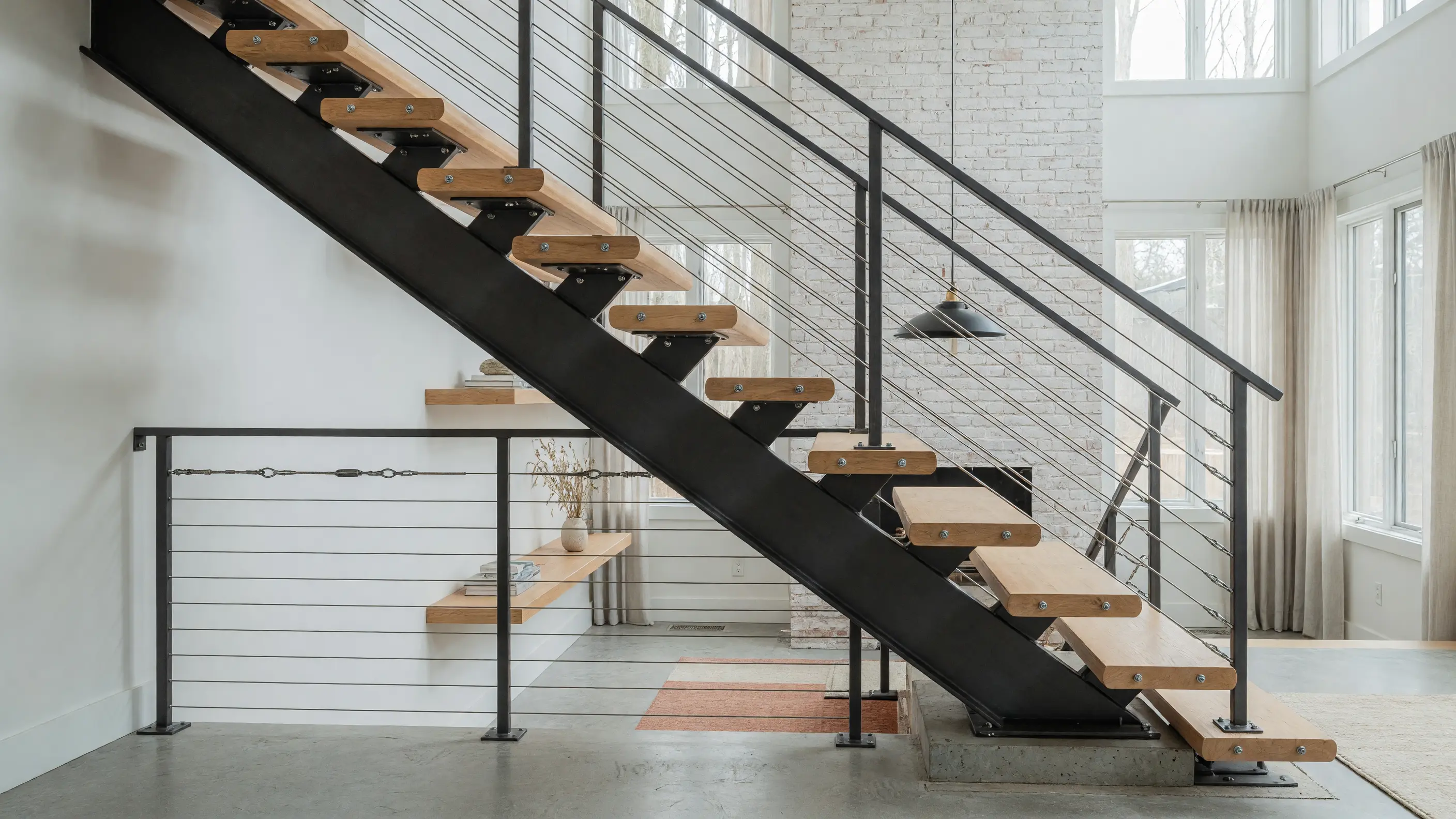 Steel mono-stringer staircase with open wood treads and matching rail in a bright modern interior